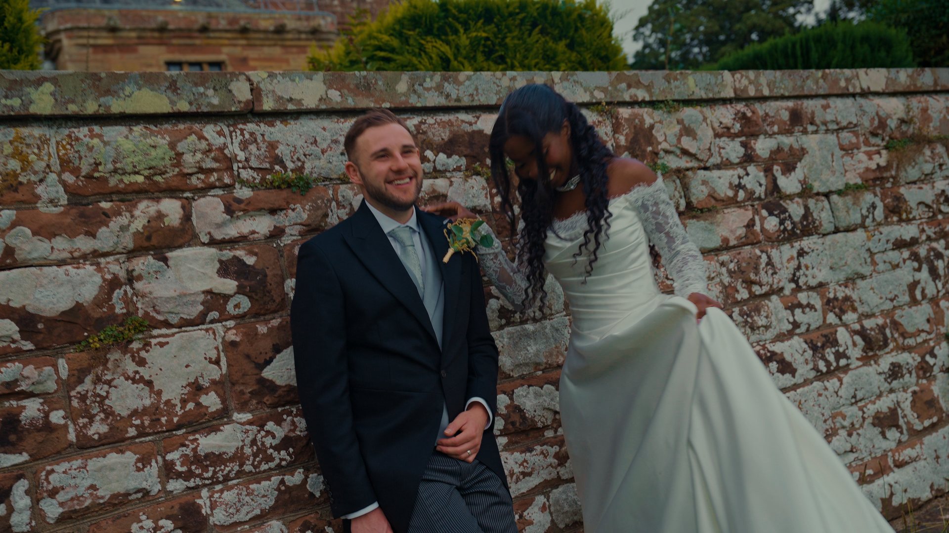 A couple laughing against a stone wall