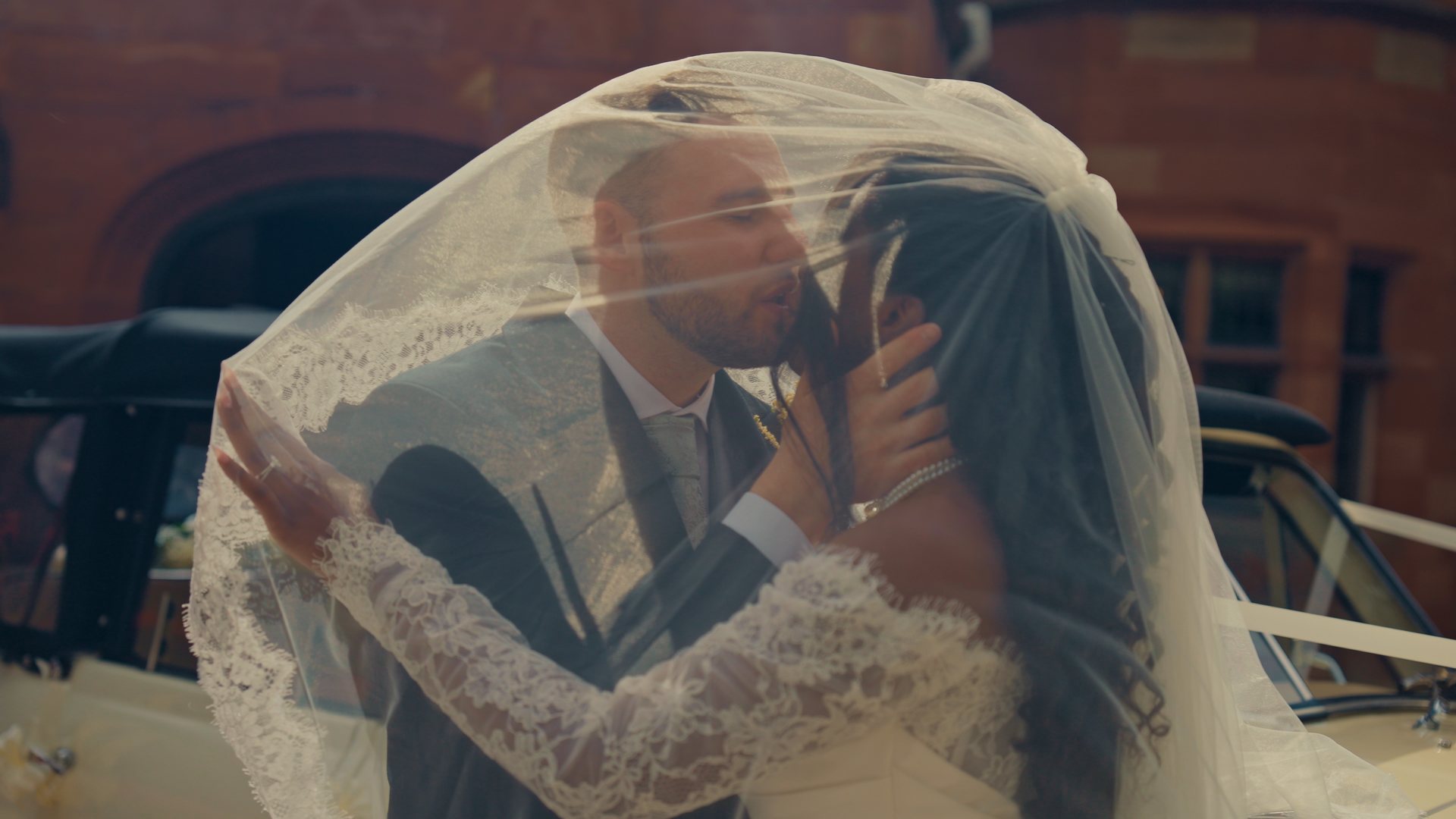 A kiss beneath the veil by the wedding car